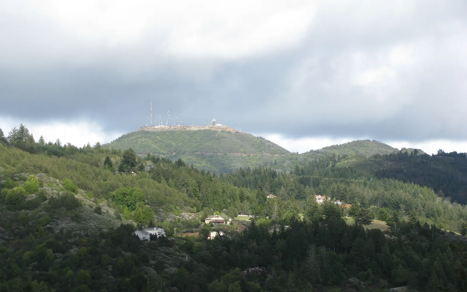 A snow-covered mountain peak in the distance under a blue sky, showing the western flank of Loma Prieta mountain in the Santa Cruz Mountains